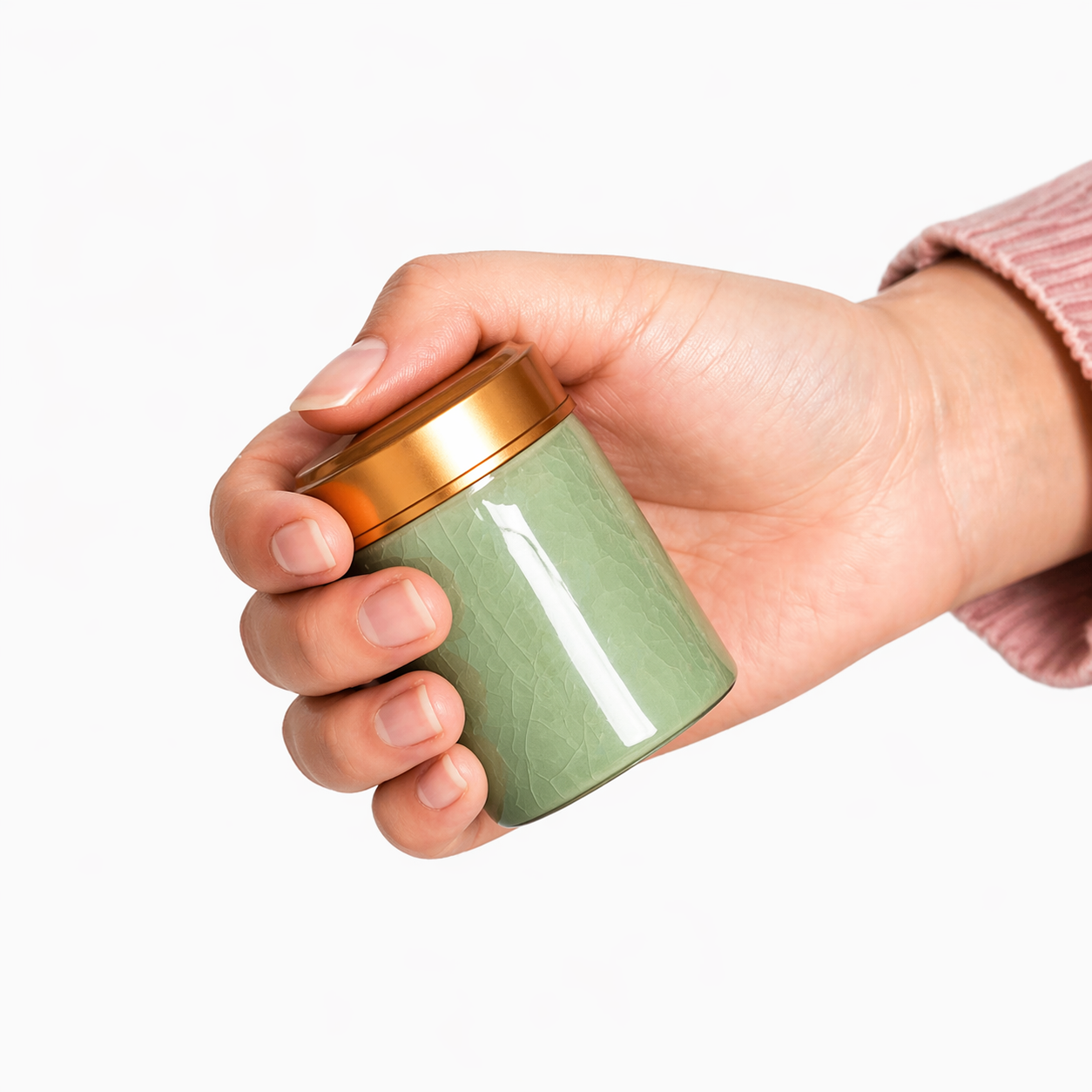 Hand holding a green container with a gold lid on a white background